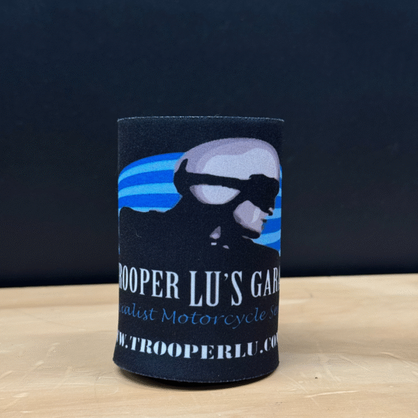 The TROOPER LU'S GARAGE STUBBY COOLER features a black design with a helmeted figure graphic, "TROOPER LU'S GARAGE" text, and www.trooperlu.com displayed on it, shown resting on a wooden surface.