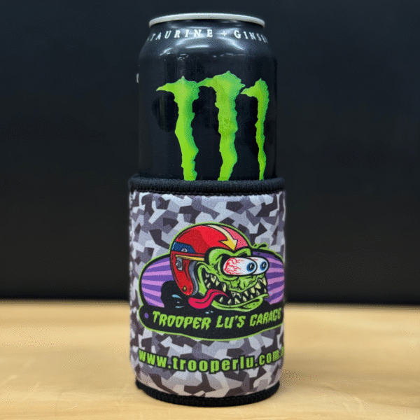 A TROOPER LU'S GARAGE STUBBY COOLER in grey camo, featuring a cartoon monster with a helmet and “Trooper Lu’s Garage www.trooperlu.com” text, holds a can of Monster Energy drink.