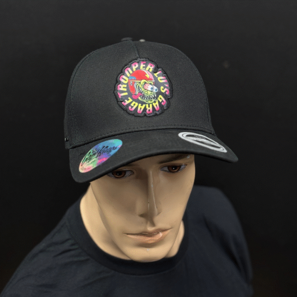 A mannequin wears TLG's UFLEX PRO STYLE SNAPBACK CAP BLACK, featuring a colorful "Space Trooper LUS Garage" patch on the front and stickers on the brim.