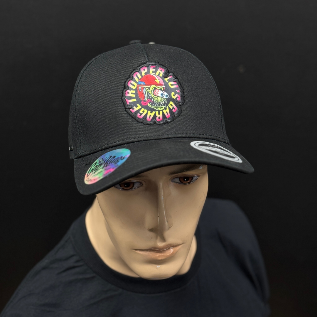A mannequin wears TLG's UFLEX PRO STYLE SNAPBACK CAP BLACK, featuring a colorful "Space Trooper LUS Garage" patch on the front and stickers on the brim.