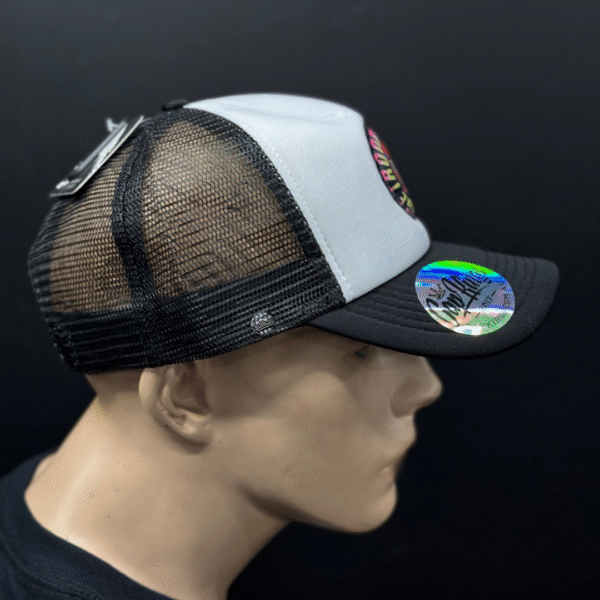 A mannequin head displays TLG's UFLEX Snap Back Trucker Cap in black/white mesh, featuring a round brim sticker and product tags on the back.