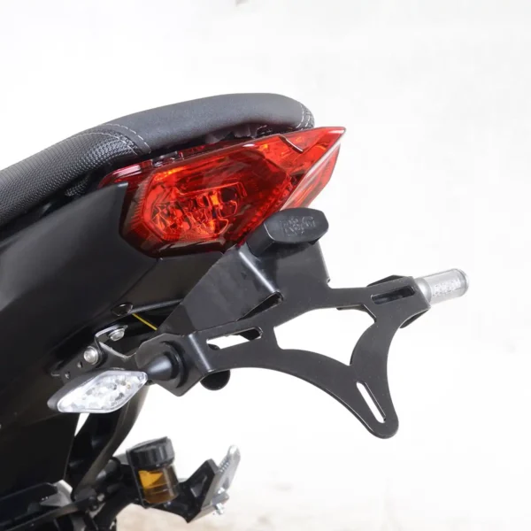 A close-up of the rear section of a motorcycle, featuring the R&G Tail Tidy for 2021-2023 MT09 (SP) with its red tail light, black mounting bracket, and small side indicators against a plain background.