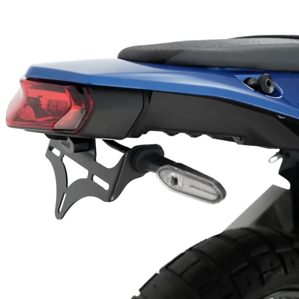 Close-up of the rear section of a motorcycle featuring the R&G Tail Tidy for Yamaha 19-24 Tenere 700, showcasing a blue seat, red taillight, metal bracket with an attached small light, and a tire.