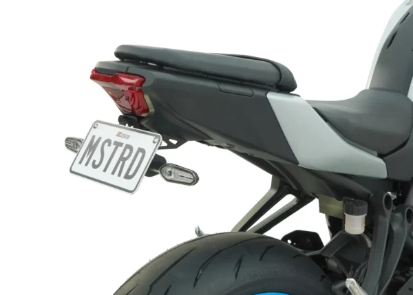 A close-up showcases the rear of a motorcycle, featuring the seat, tire, and license plate with "MSTRD" text. This scene includes the MUSTARD MT-07 2025 TAIL TIDY - 186MM against a white backdrop.